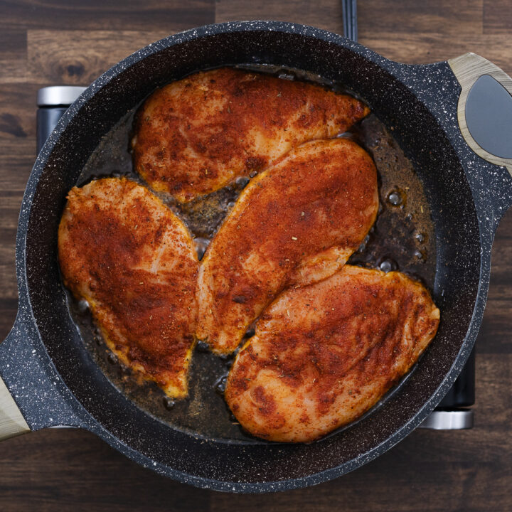 A heavy-bottomed skillet with the seasoned chicken breasts placed for searing.