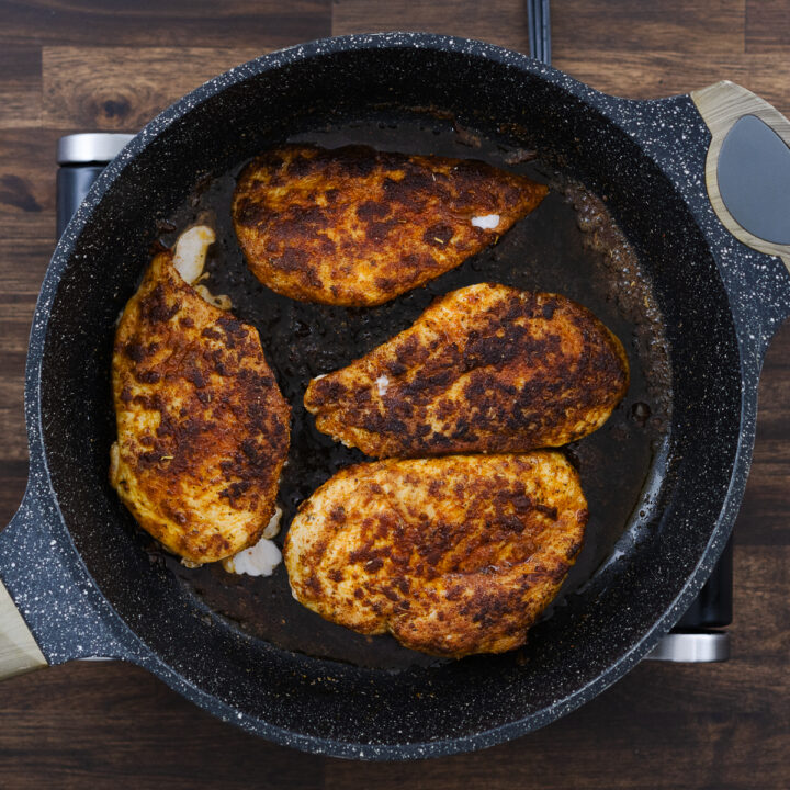 The chicken breasts in the pan, seared to a golden brown on the outside.