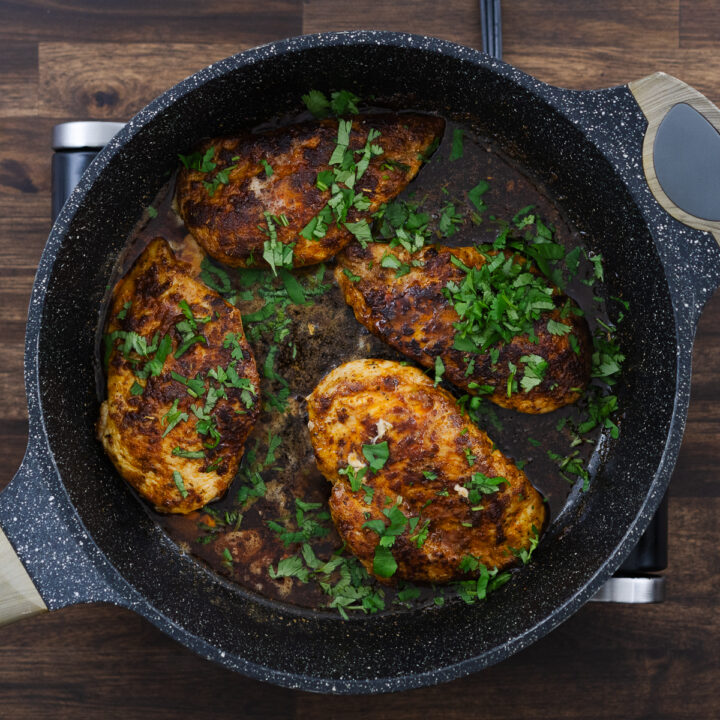 Pan-seared chicken breasts garnished with freshly chopped cilantro leaves.