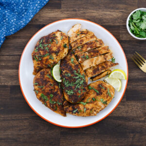 Pan-seared chicken breasts served on a plate, garnished with cilantro and lime slices.