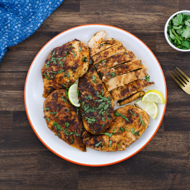 Pan-seared chicken breasts served on a plate, garnished with cilantro and lime slices.